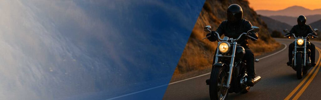 A view of two cruiser motorcycles along a winding, two-lane road at sunset.