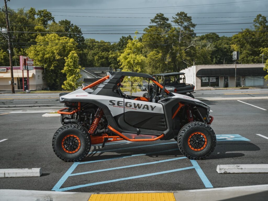 Off-road Segway vehicle with orange frame parked in a handicapped parking space, black body and large tires.