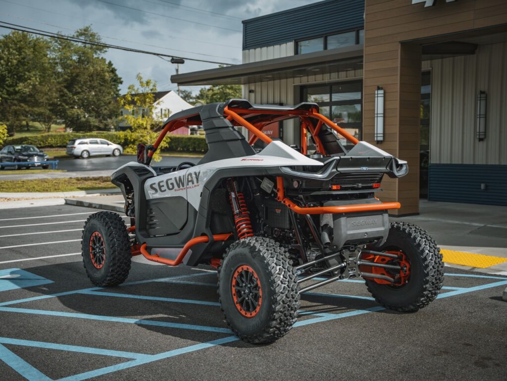 Off-road Segway vehicle with orange frame parked in a handicapped parking space outside a storefront building.