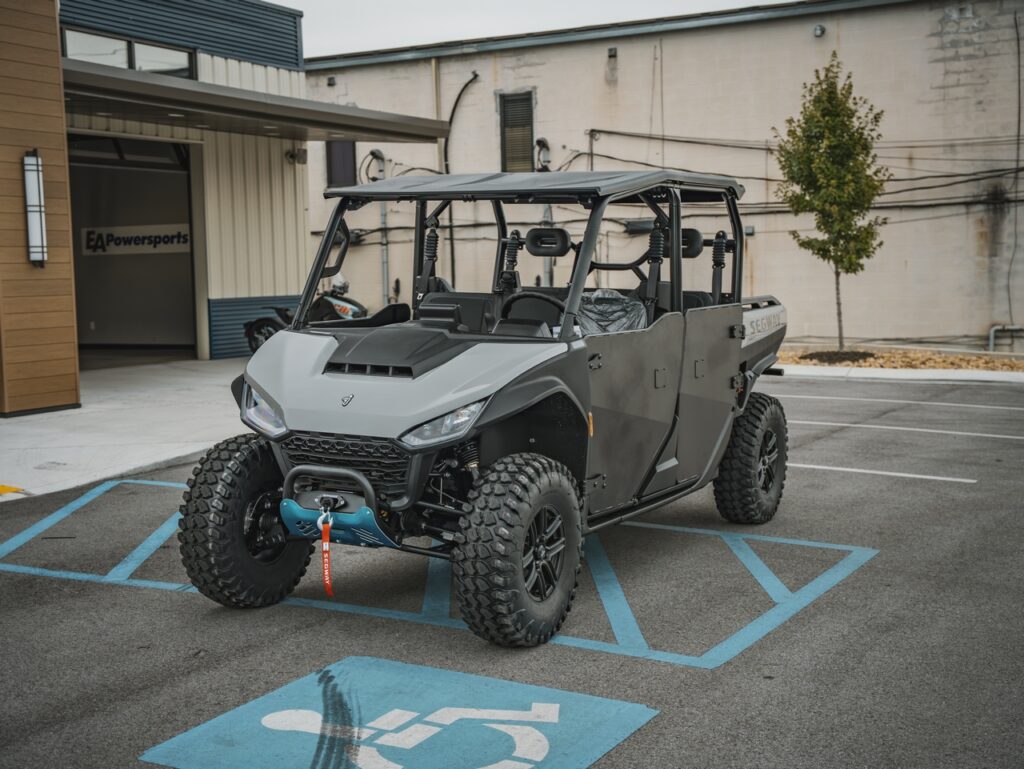 Gray off-road utility vehicle with a roll cage parked in a disabled parking space outside EA Powersports store.