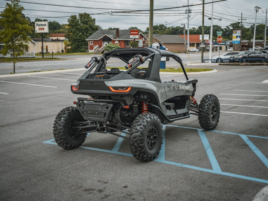 Gray off-road side-by-side UTV with oversized tires and orange suspension, parked in a lot.