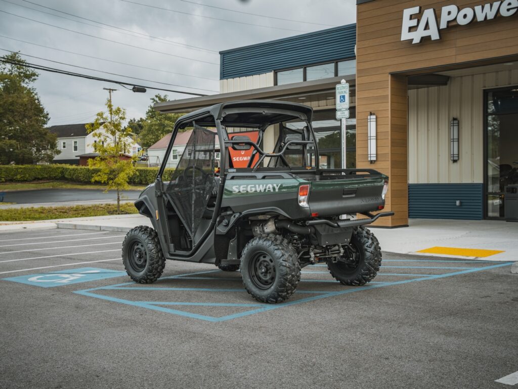 Dark green off-road utility vehicle labeled SEGWAY parked in a handicap space near a storefront with an EA Power sign behind it.