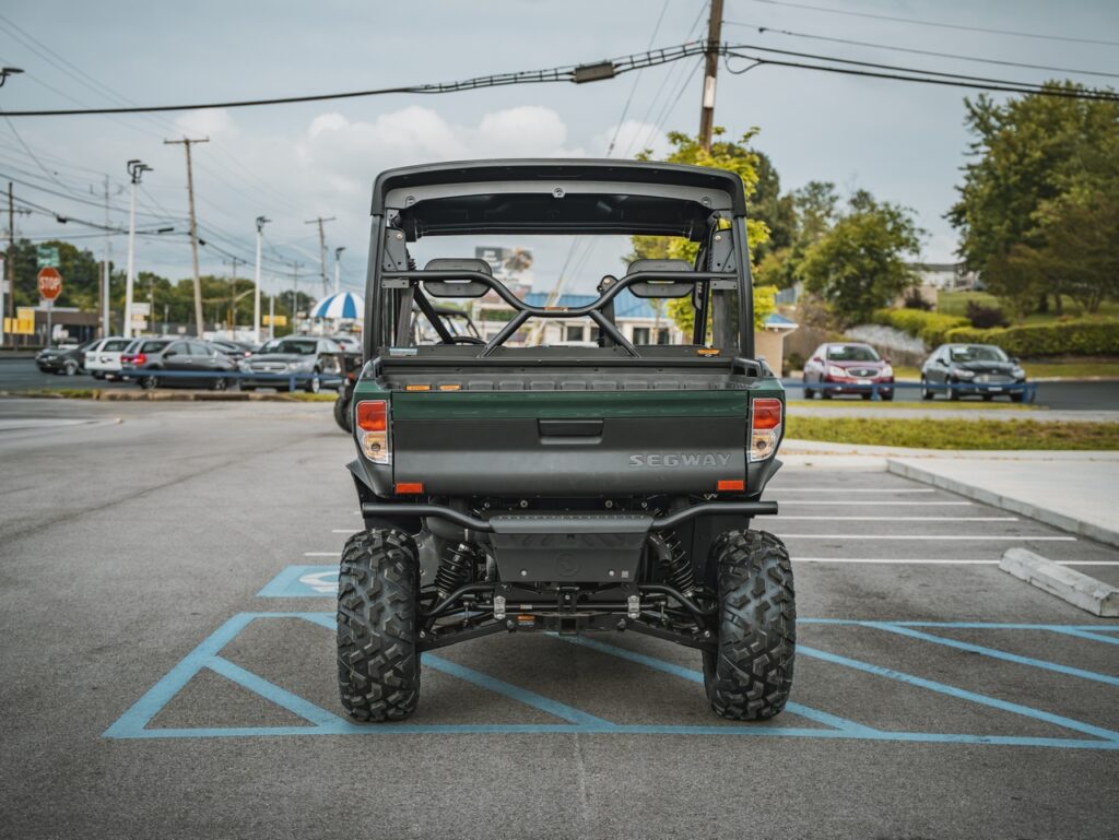 Rear view of a Segway off-road utility vehicle parked in a blue-striped handicapped space, showing large tires and roll cage.