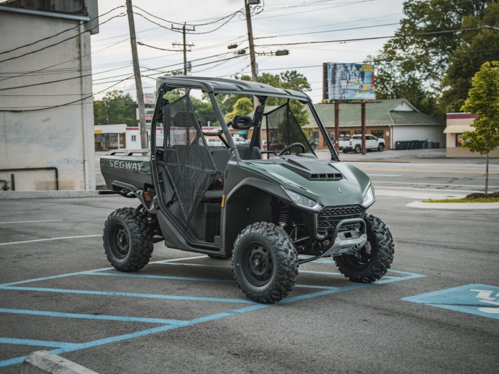 Green Segway off-road utility vehicle with a roll cage and mesh doors parked in a handicapped parking space in a parking lot.