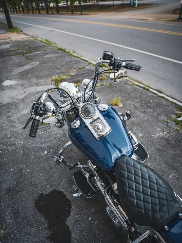 Blue motorcycle parked on a street, showing a shiny chrome finish, diamond-stitched black seat, and chrome handlebars with mirrors.