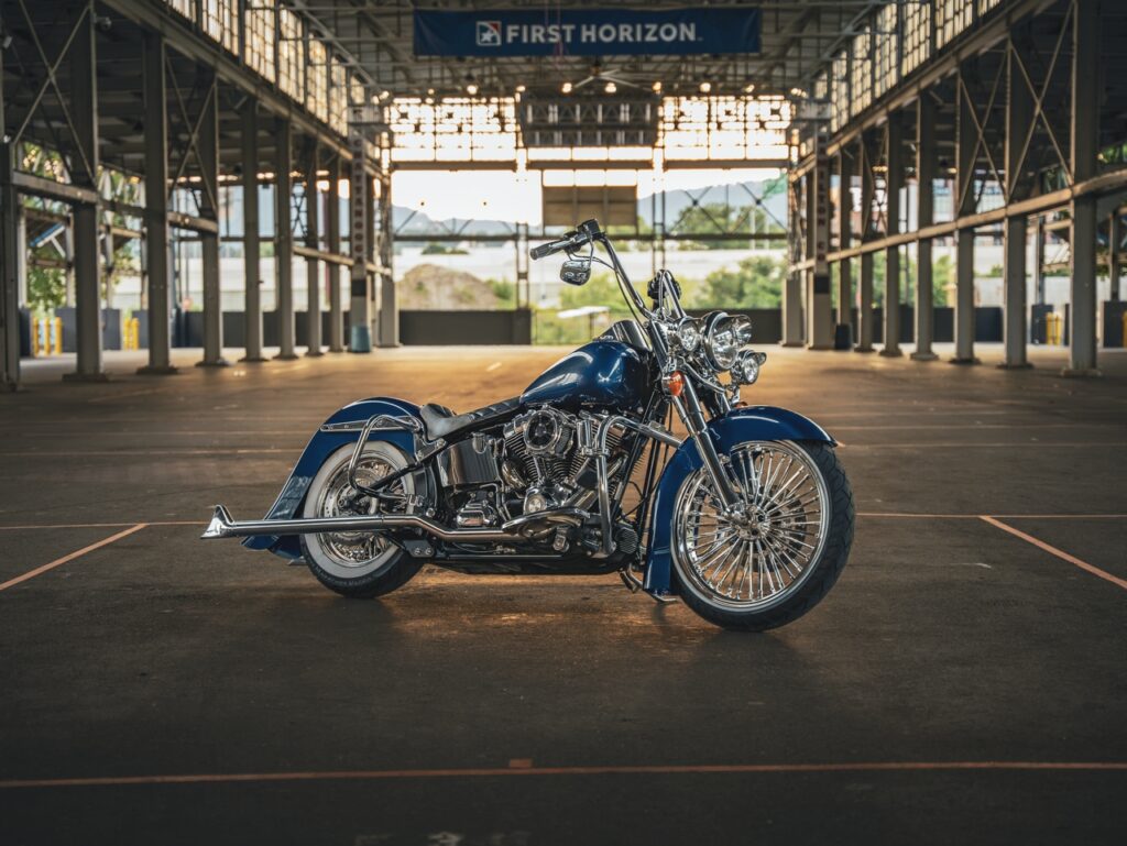 Blue cruiser motorcycle with chrome details parked in a dimly lit, open-span parking structure under a First Horizon banner.